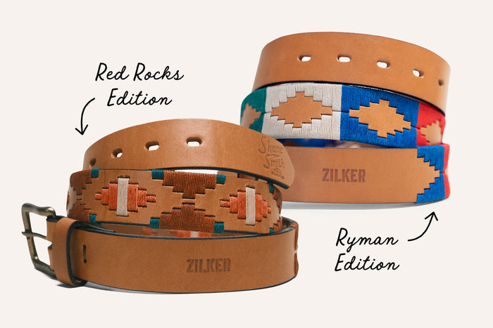 Two separate collaboration belts with Shane Smith and the Saints are picture. The first features burnt orange, teal, cream, and orange stitching on a premium light brown leather. The second features cream, royal blue, red, and teal stitching on a premium light brown leather.