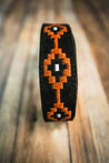 Close-up of the Zilker Belts Texas Exes II wristband, crafted from black Argentine suede leather with striking orange and white geometric patterns, displayed on a wooden surface.