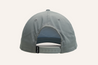 The image shows the back view of a grey Zilker Sessions Imperial Hat from Zilker Belts with an adjustable snap closure. A black tag with white text is attached to one side of the snap closure.