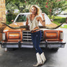 a woman in Zilker Belts cowboy boots posing next to an old car.