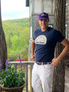 A man standing on a porch wearing Zilker Belts Argentina hat and white pants.