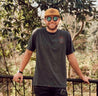 A man wearing Zilker Belts NOLA Rope Hat and a t - shirt standing in a wooded area.