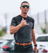 A man in a black shirt and sunglasses is walking in a parking lot, wearing Zilker Belts' Verde.