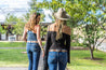 Two girls wearing leather belts. One wears a light brown leather belt with black and white stitching.